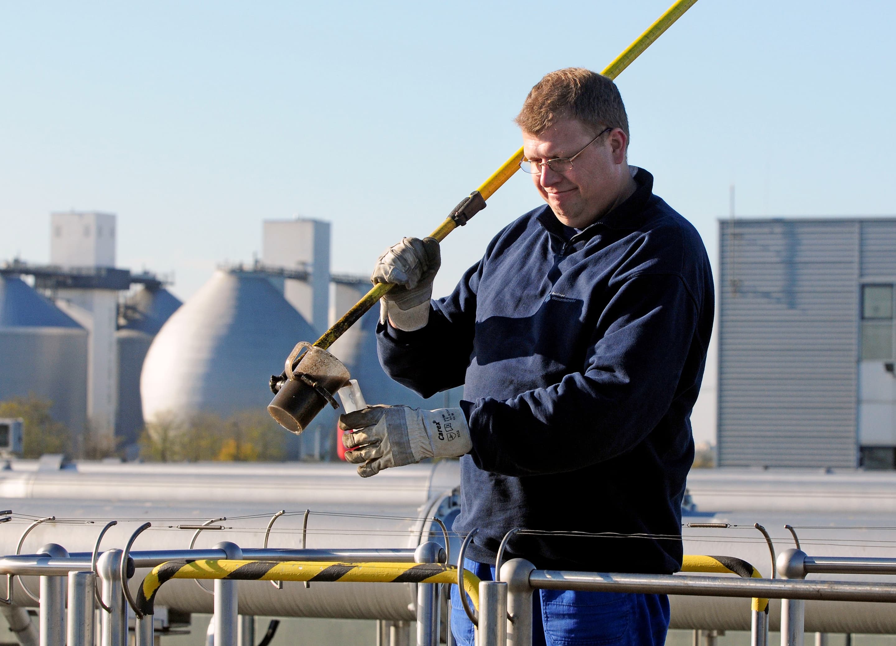Ein Mitarbeiter einer Kläranlage nimmt eine Wasserprobe aus einem Klärbecken.
