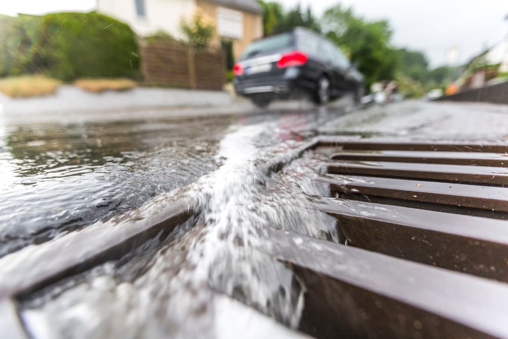 Regenwasser fließt bei starkem Regen in einen Straßenkanal.