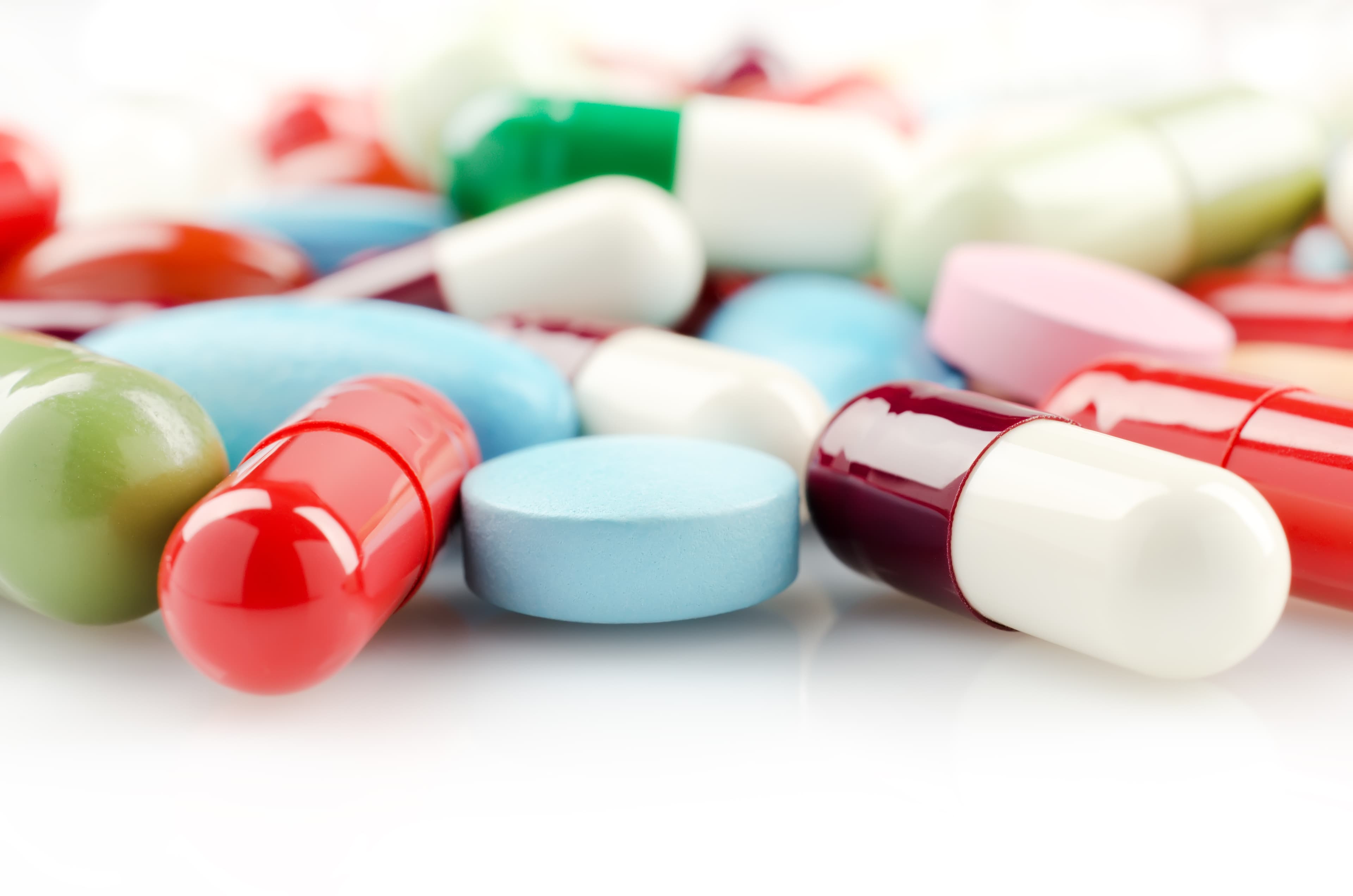 Bunte Tabletten und Pillen liegen lose zerstreut auf weißem Grund.